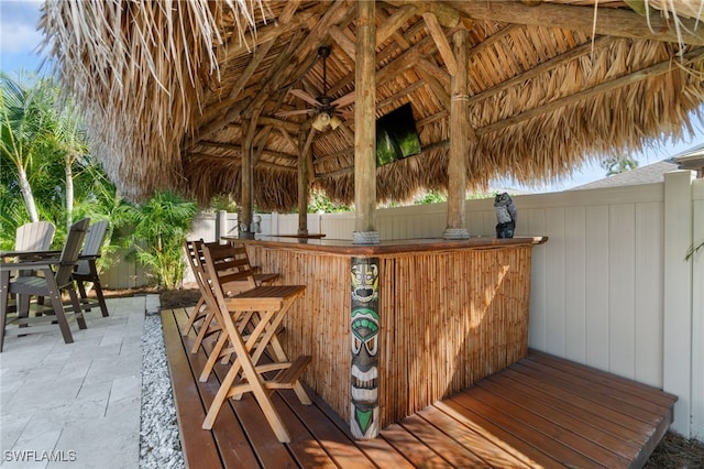 wooden terrace with a ceiling fan, outdoor dry bar, fence, a gazebo, and a patio area