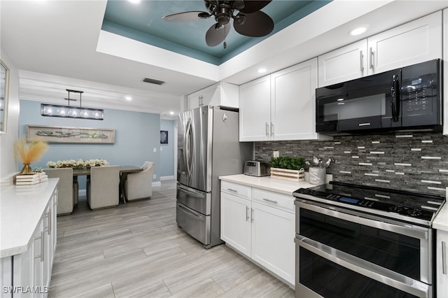 kitchen with white cabinets, light countertops, appliances with stainless steel finishes, a tray ceiling, and tasteful backsplash