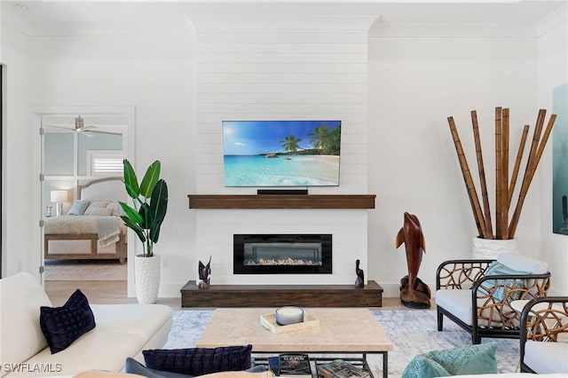 living area with ceiling fan, a fireplace, wood finished floors, and crown molding