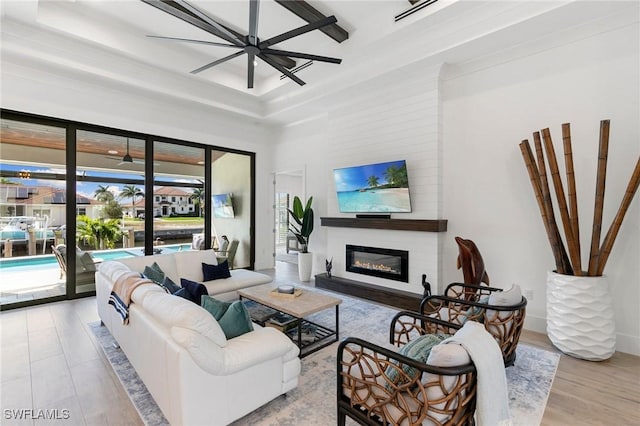 living room featuring baseboards, a ceiling fan, a glass covered fireplace, wood finished floors, and a tray ceiling