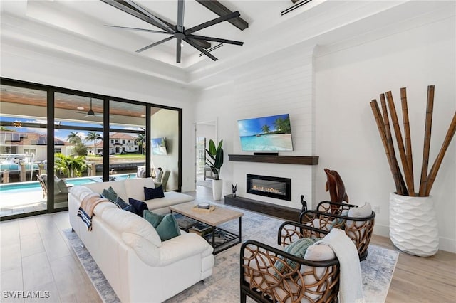 living area with a tray ceiling and a glass covered fireplace
