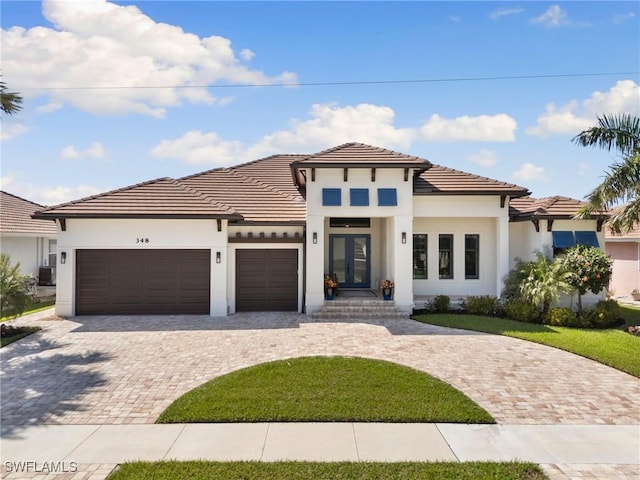 view of front of property with a tile roof, an attached garage, decorative driveway, french doors, and stucco siding