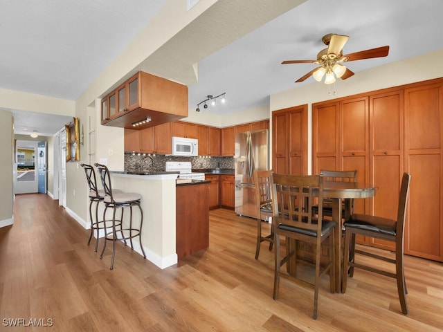 kitchen featuring white appliances, light wood finished floors, brown cabinetry, decorative backsplash, and a peninsula