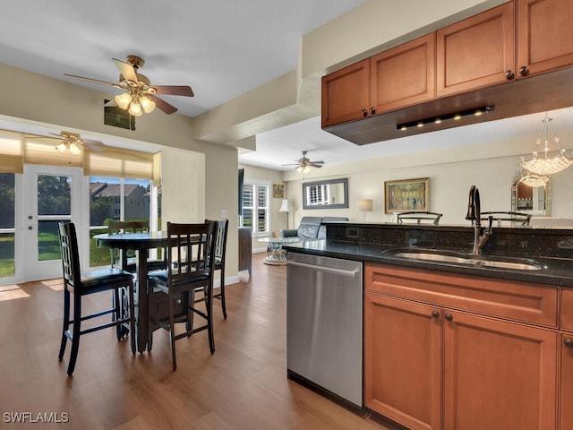 kitchen featuring light wood finished floors, brown cabinetry, a ceiling fan, stainless steel dishwasher, and a sink