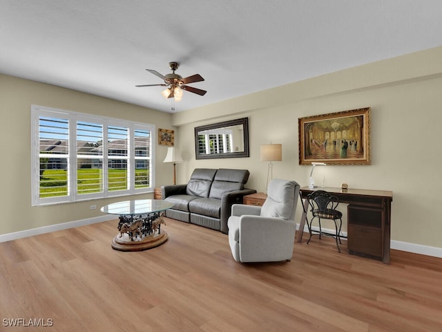 living area with baseboards, a ceiling fan, and light wood-style floors