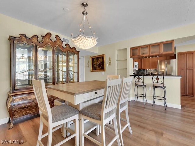 dining space with a chandelier, light wood finished floors, and baseboards