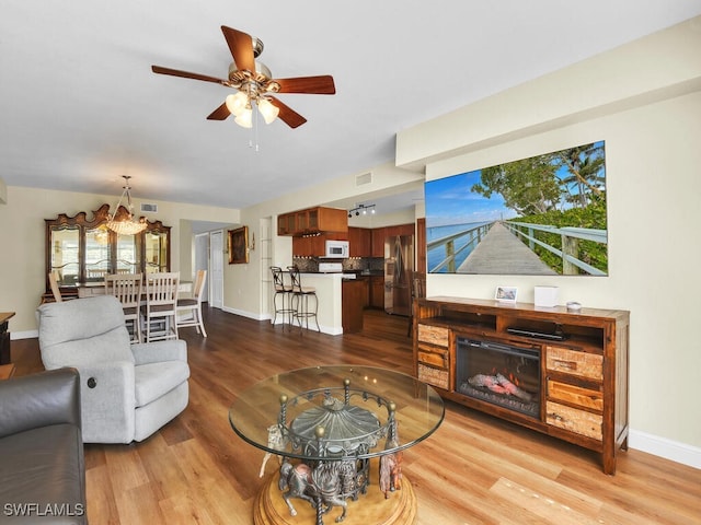 living area with visible vents, a glass covered fireplace, ceiling fan, wood finished floors, and baseboards