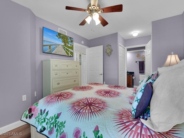 bedroom featuring wood finished floors, visible vents, a ceiling fan, baseboards, and ensuite bath