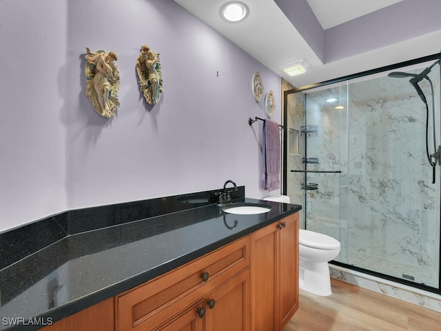 bathroom featuring toilet, a marble finish shower, wood finished floors, and vanity