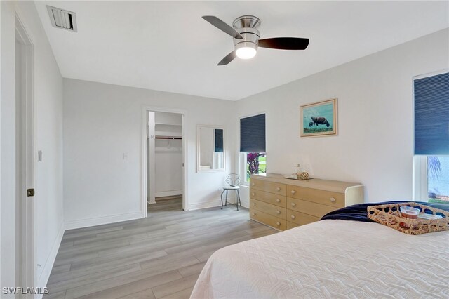 bedroom with visible vents, baseboards, a ceiling fan, light wood-style flooring, and a walk in closet