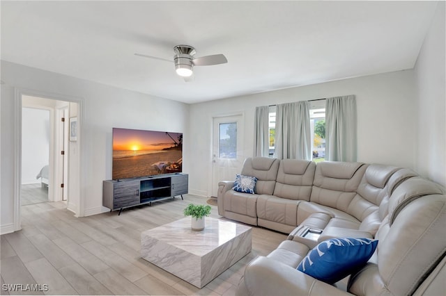 living room with ceiling fan, baseboards, and light wood-style floors