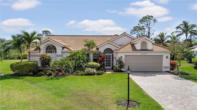 mediterranean / spanish-style house featuring a garage, a tile roof, decorative driveway, stucco siding, and a front lawn