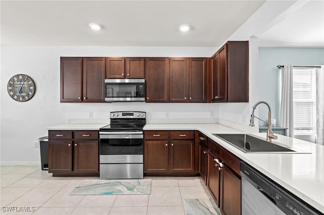 kitchen featuring light tile patterned floors, stainless steel appliances, a sink, dark brown cabinets, and light countertops