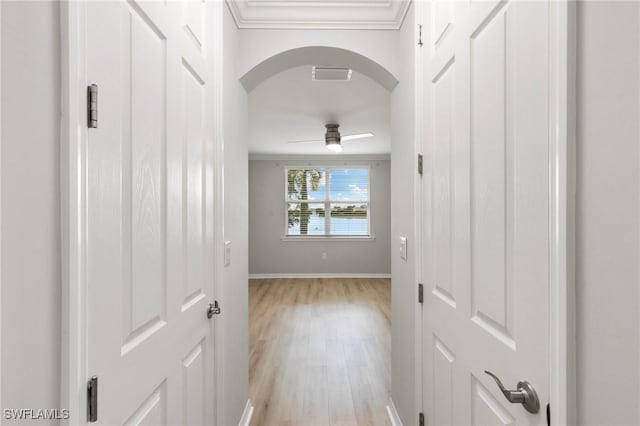 hallway with baseboards, visible vents, arched walkways, ornamental molding, and light wood-style floors