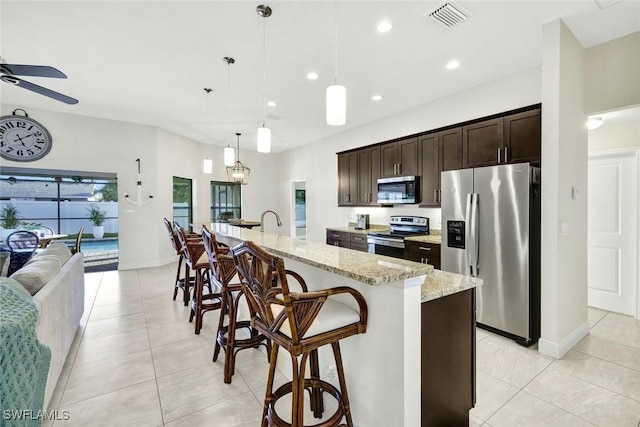 kitchen with a breakfast bar, stainless steel appliances, visible vents, open floor plan, and dark brown cabinetry