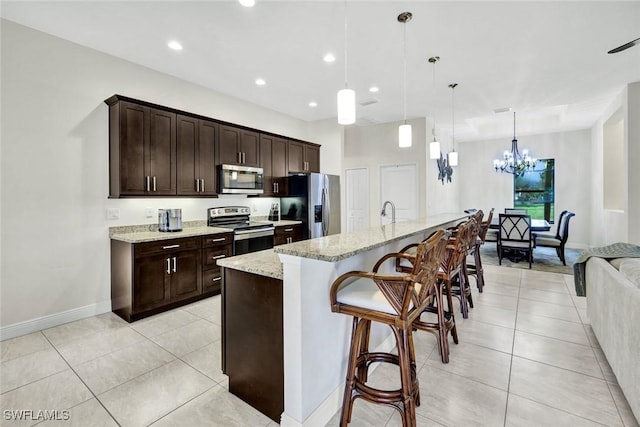 kitchen featuring dark brown cabinetry, light stone counters, a breakfast bar, stainless steel appliances, and light tile patterned flooring