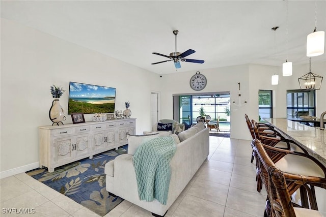 living area with ceiling fan with notable chandelier, baseboards, and light tile patterned floors