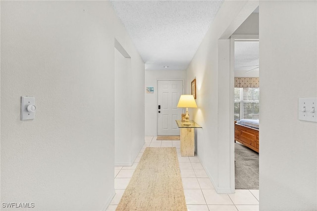 hallway featuring a textured ceiling, light tile patterned floors, and baseboards