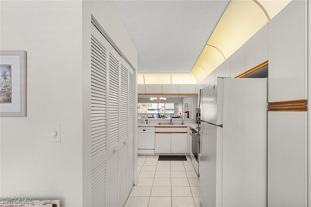 kitchen with white appliances, light tile patterned floors, an inviting chandelier, light countertops, and white cabinetry