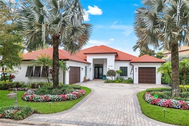 mediterranean / spanish-style home featuring stucco siding, an attached garage, a tile roof, and decorative driveway