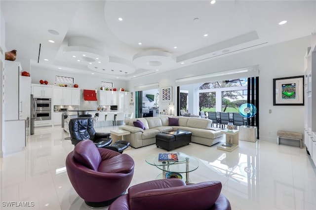 living area with baseboards, a tray ceiling, light tile patterned floors, recessed lighting, and a towering ceiling