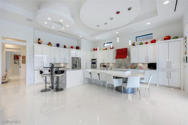 kitchen with a kitchen bar, appliances with stainless steel finishes, a raised ceiling, and a towering ceiling