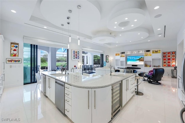 kitchen featuring beverage cooler, a tray ceiling, a sink, a large island, and stainless steel dishwasher