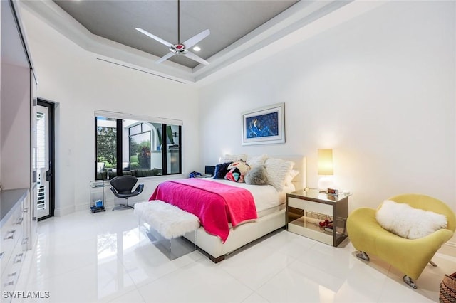 bedroom featuring baseboards, a high ceiling, light tile patterned flooring, ceiling fan, and a raised ceiling