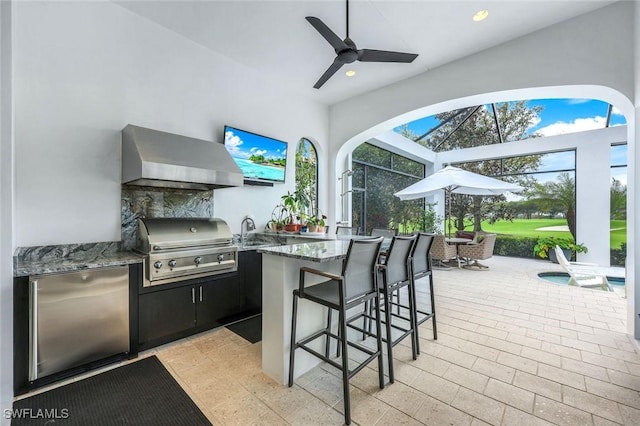 view of patio / terrace featuring ceiling fan, a lanai, outdoor wet bar, area for grilling, and an outdoor kitchen