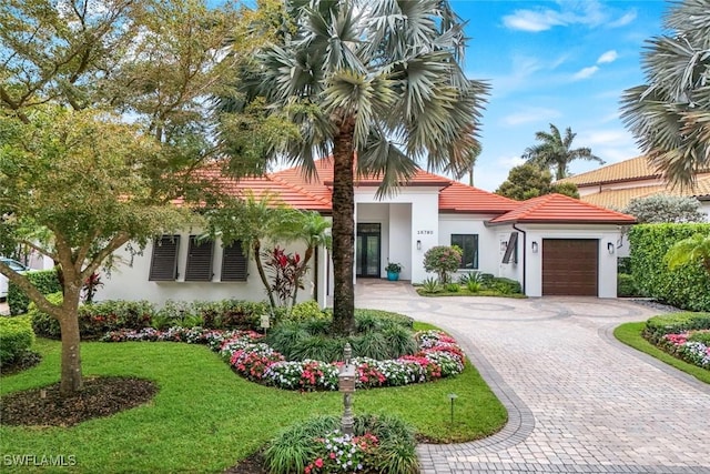 mediterranean / spanish house featuring a tiled roof, decorative driveway, a garage, and stucco siding