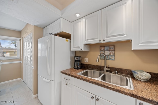 kitchen featuring light tile patterned floors, a sink, white cabinets, freestanding refrigerator, and dark countertops