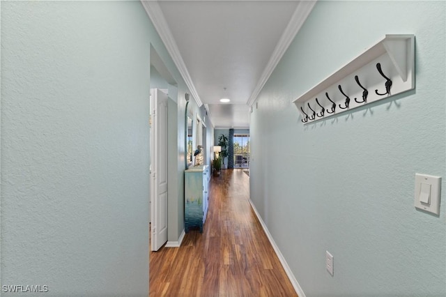 hall featuring a textured wall, baseboards, crown molding, and wood finished floors