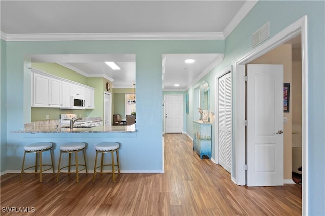 kitchen with a kitchen bar, wood finished floors, visible vents, and crown molding