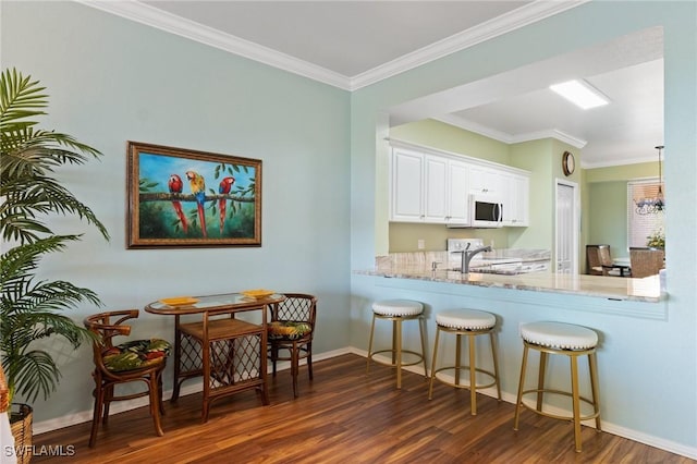 kitchen featuring white microwave, dark wood-type flooring, ornamental molding, a sink, and a kitchen bar