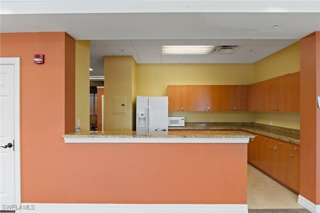 kitchen featuring a peninsula, white appliances, brown cabinetry, and light stone countertops