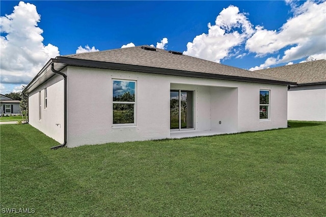 rear view of house featuring roof with shingles, a lawn, and stucco siding