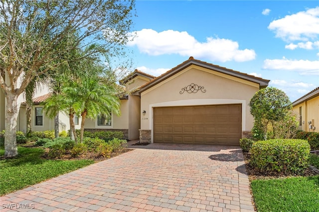 mediterranean / spanish home with an attached garage, stone siding, decorative driveway, and stucco siding