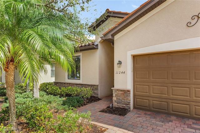 property entrance featuring an attached garage, stone siding, a tiled roof, and stucco siding