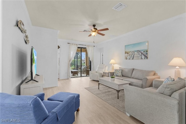 living area featuring ornamental molding, light wood finished floors, visible vents, and a ceiling fan