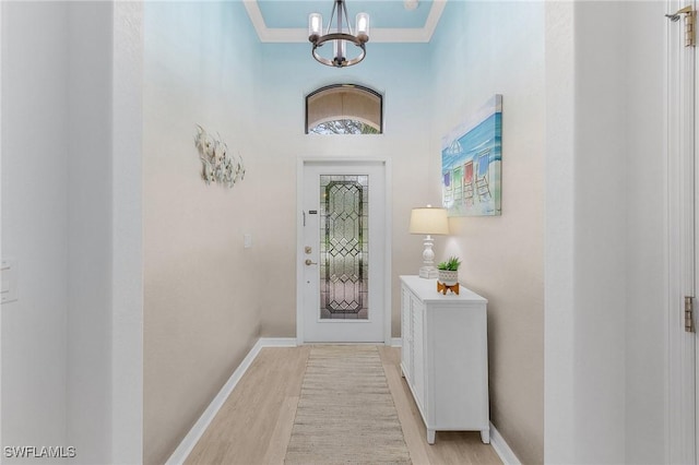 doorway featuring light wood finished floors, baseboards, crown molding, and an inviting chandelier