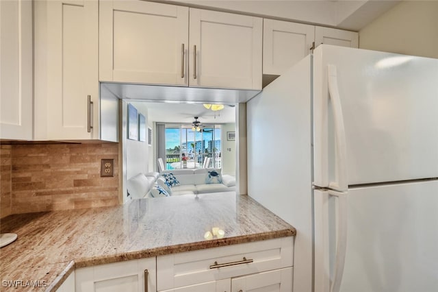 kitchen featuring tasteful backsplash, white cabinets, a ceiling fan, light stone counters, and freestanding refrigerator