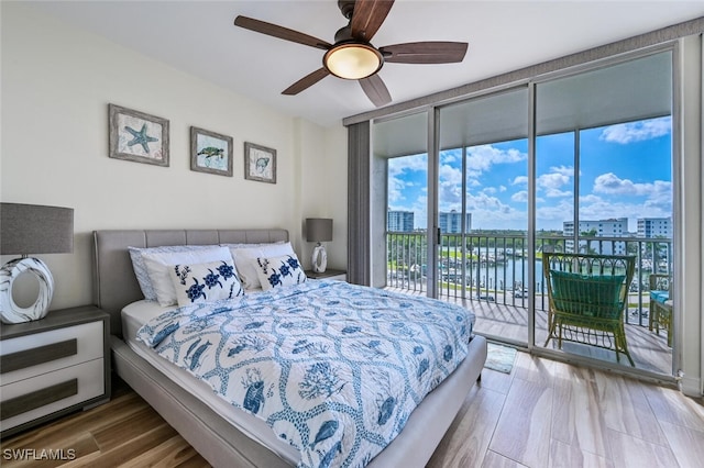 bedroom with ceiling fan, wood finished floors, access to exterior, a view of city, and a wall of windows