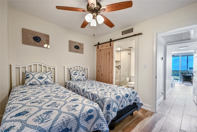 bedroom with a barn door, visible vents, ceiling fan, and wood finished floors