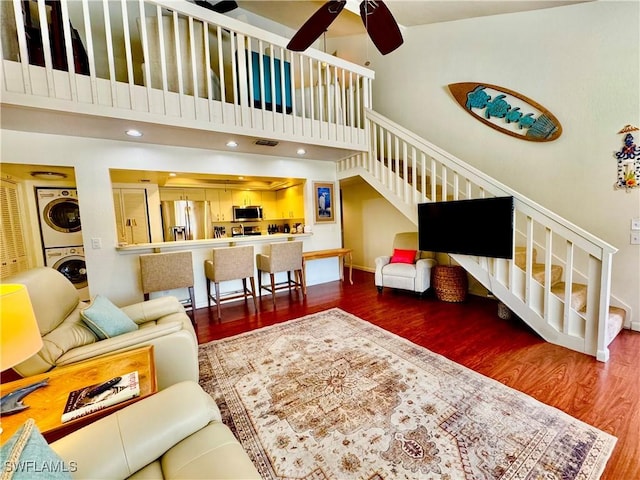 living area with stacked washer / drying machine, stairway, a high ceiling, and wood finished floors