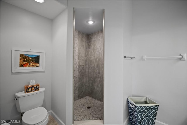 full bathroom featuring a tile shower, toilet, and baseboards