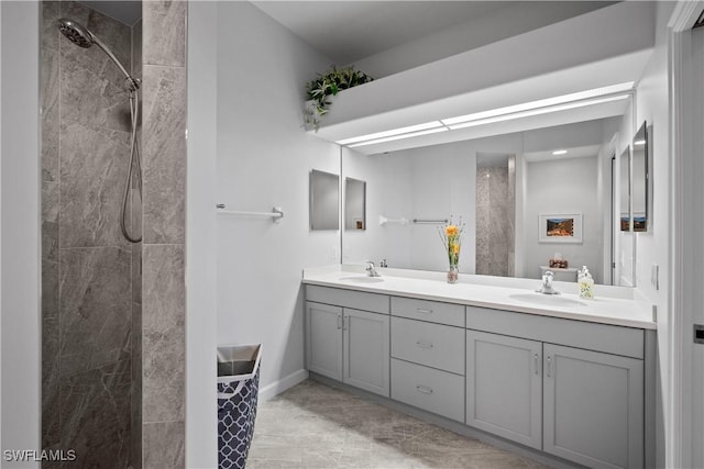 full bath featuring double vanity, baseboards, a tile shower, and a sink