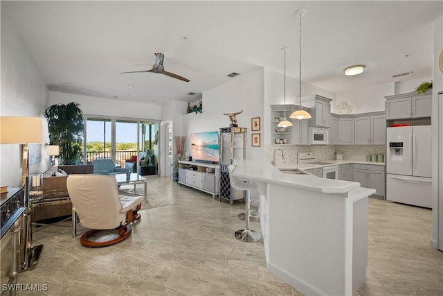 kitchen featuring a peninsula, white appliances, a sink, open floor plan, and gray cabinets