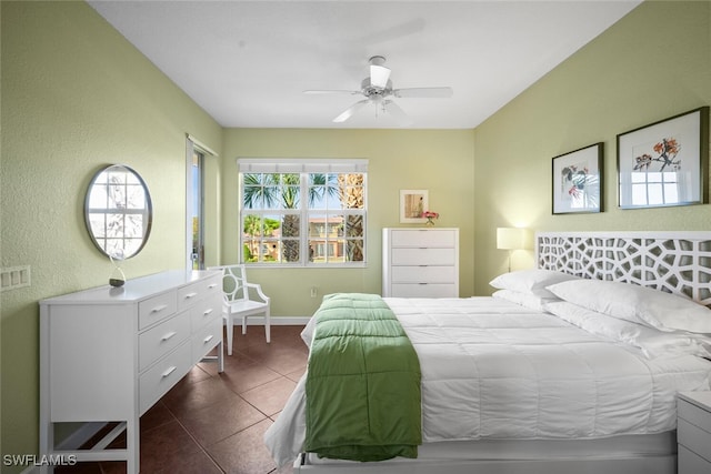 bedroom with ceiling fan, a textured wall, baseboards, and dark tile patterned flooring