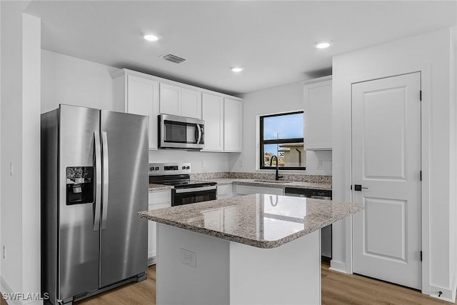 kitchen with appliances with stainless steel finishes, a sink, light wood-style floors, a kitchen island, and light stone counters