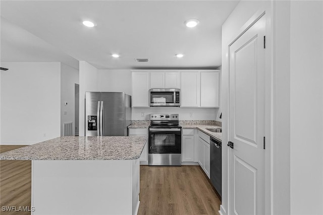 kitchen with appliances with stainless steel finishes, a center island, light stone counters, white cabinets, and recessed lighting